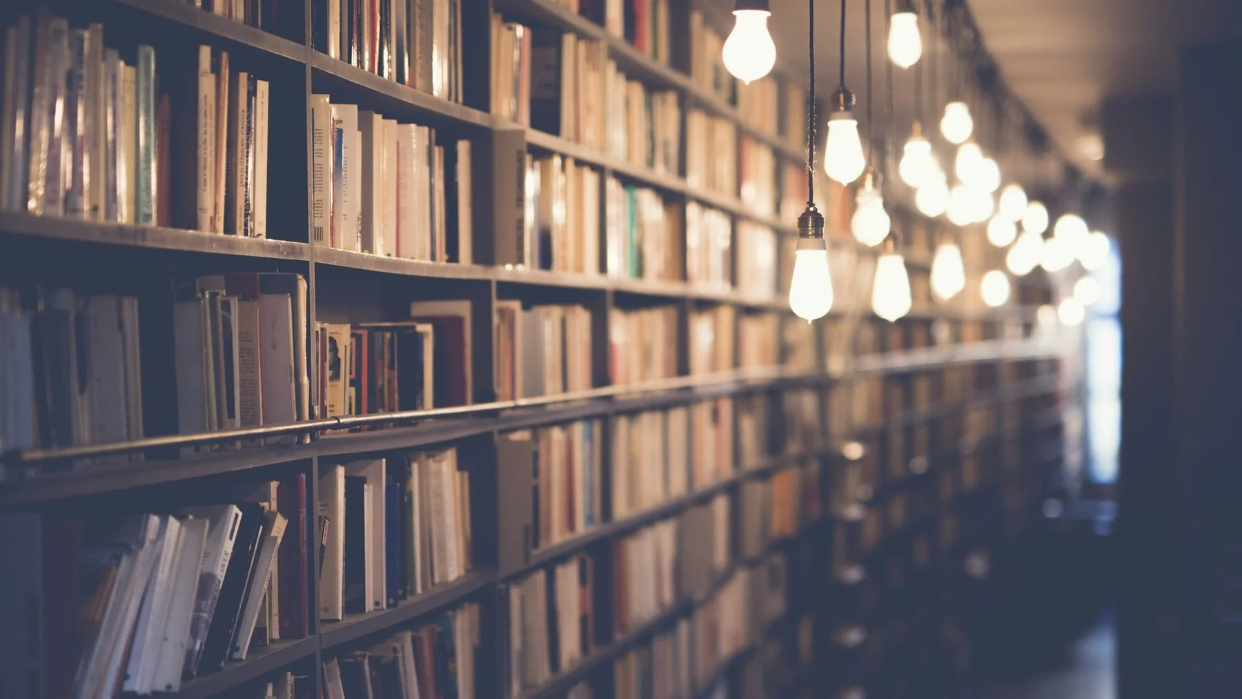 Corredor de biblioteca com estantes cheias de livros e lâmpadas acesas penduradas do teto